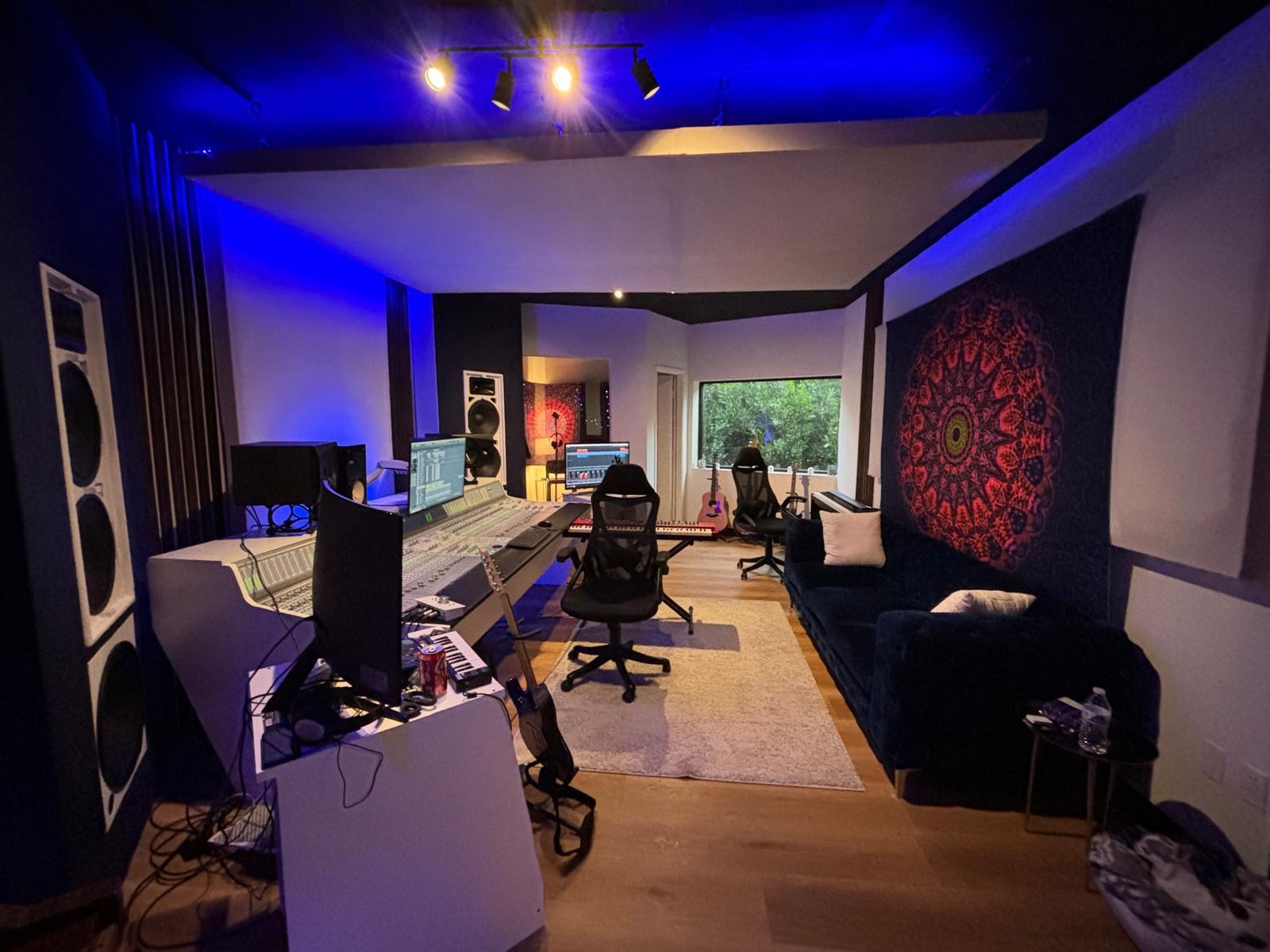Recording studio with mixing console, large monitors, seating, and blue ceiling lighting
